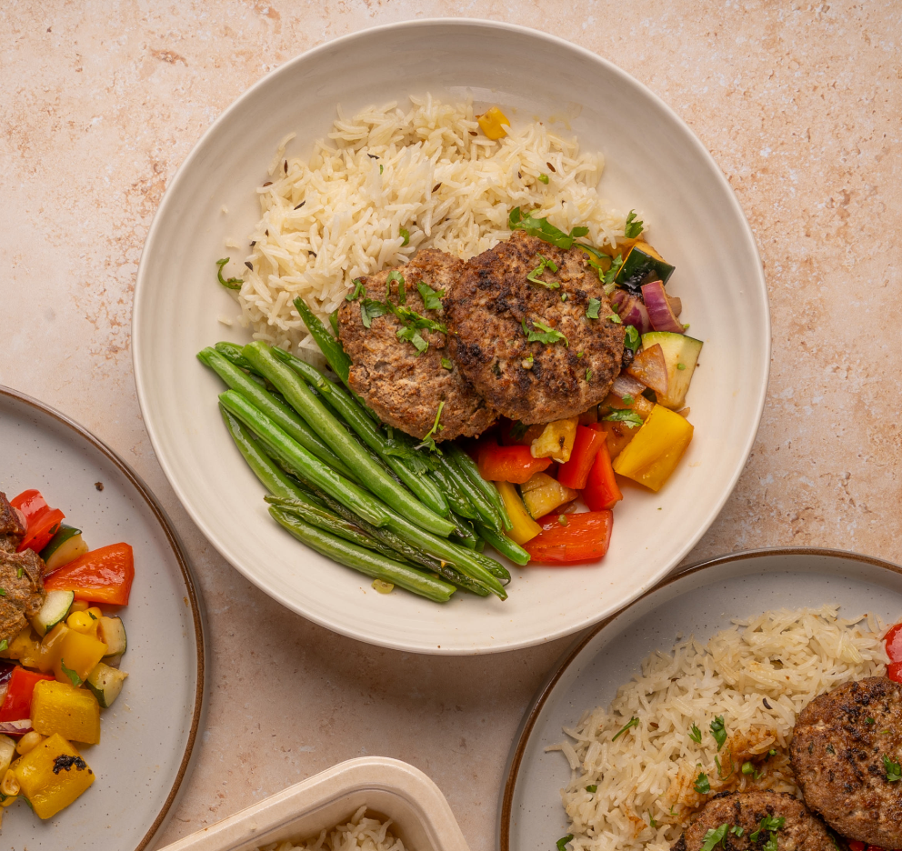 Plates of food including rice, vegetables, and meat patties on a beige surface.
