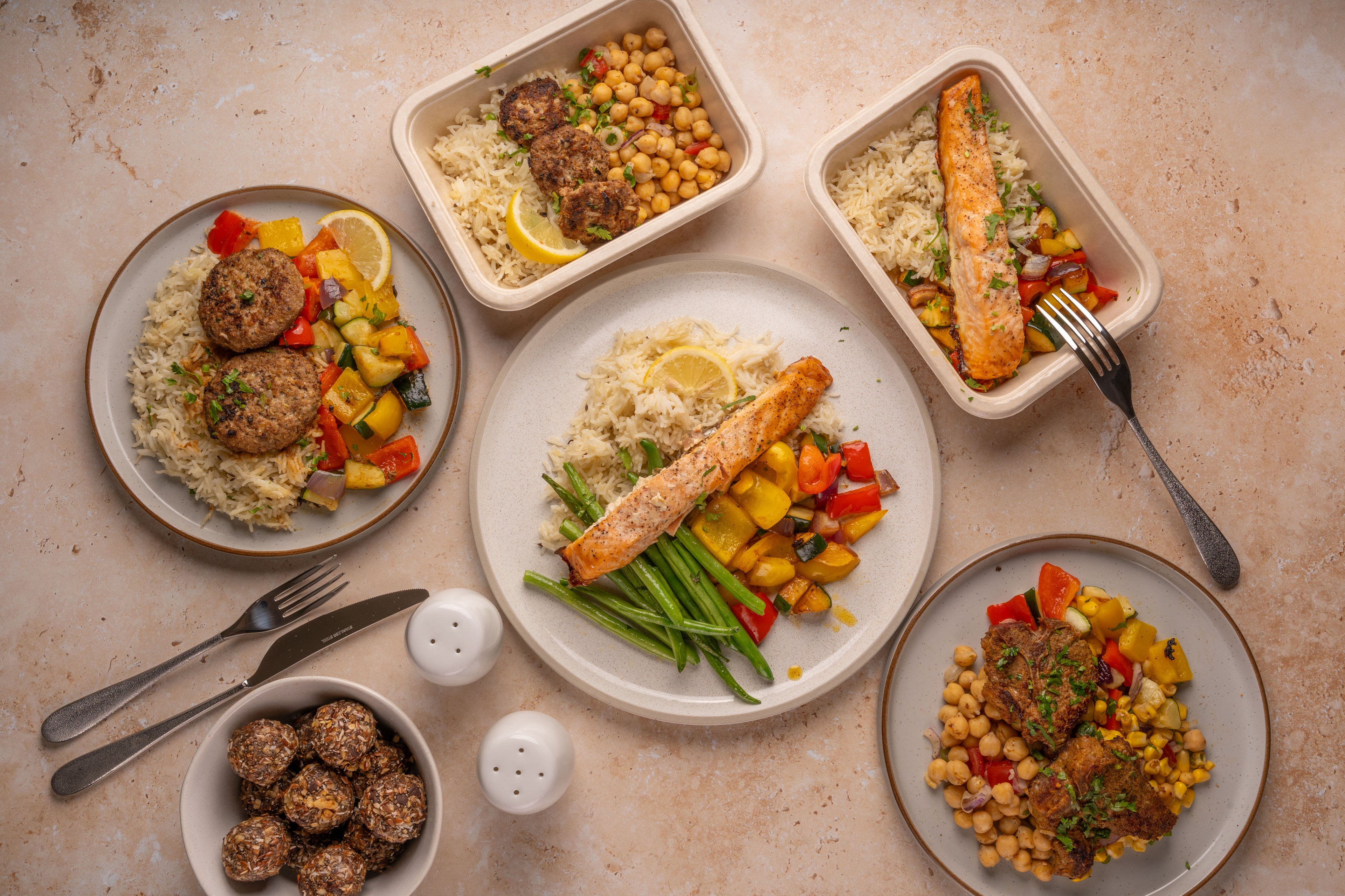 Assorted meals including salmon, vegetables, and meatballs on a beige surface.