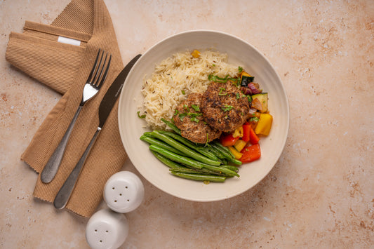 Plate of food with rice, kebabs, vegetables, and green beans on a beige surface with cutlery and napkins.