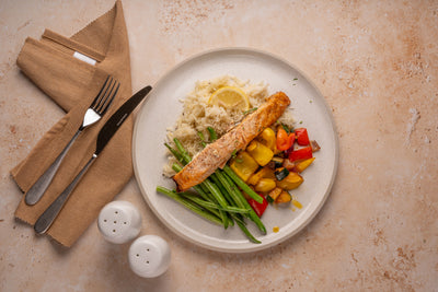 Plated meal with salmon, vegetables, and rice on a beige surface with cutlery and napkins.