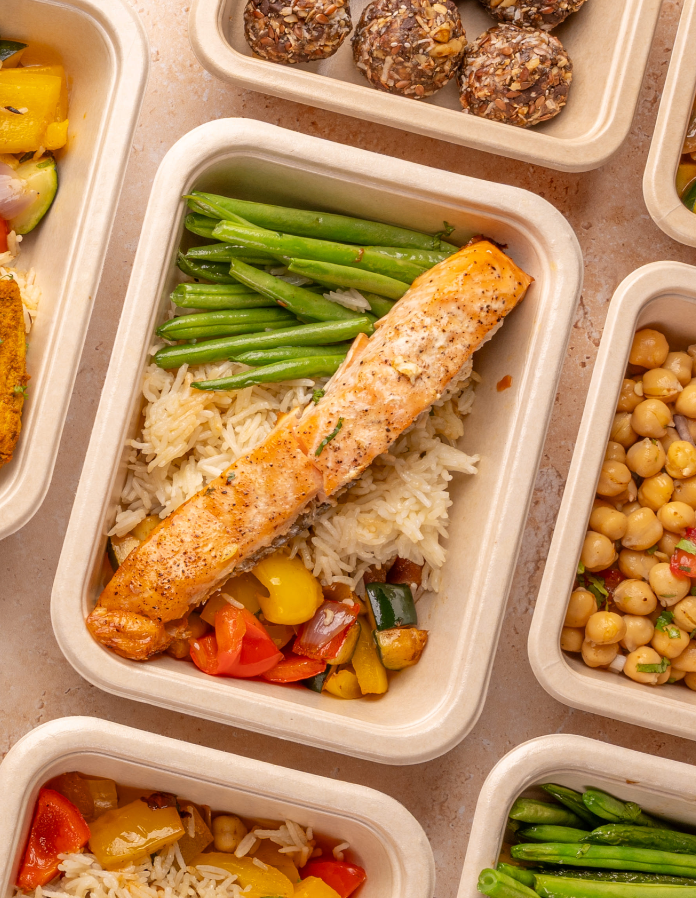 Prepared meals with salmon, green beans, rice, and vegetables in containers.